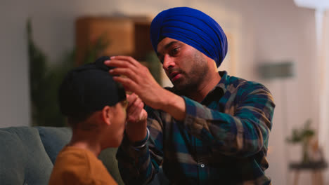 Father-Using-Salai-Needle-To-Tidy-Away-Hair-When-Tying-Turban-Onto-Head-Of-Young-Sikh-Son-Sitting-On-Sofa-Shot-in-Real-Time-1